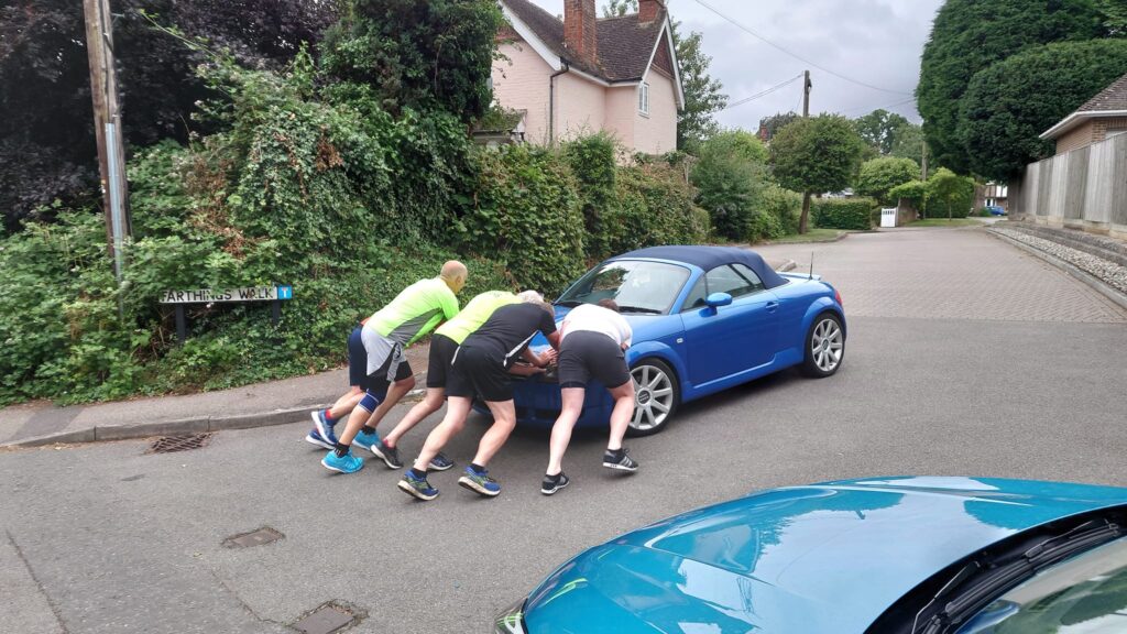 A group of runners pushing a car