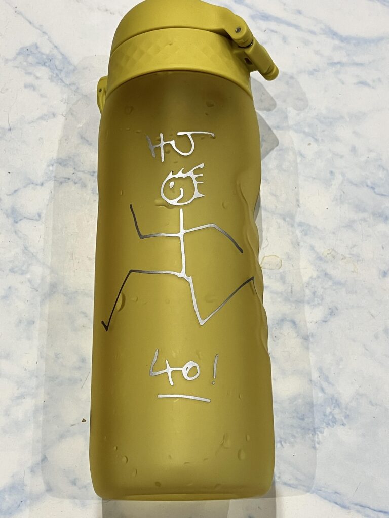 A gold water bottle with a stick man drawn on it.