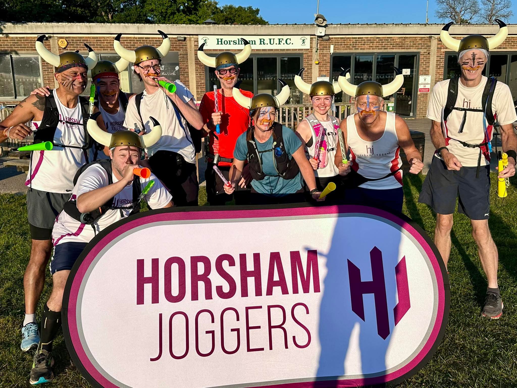 A group of runners in fancy dress behind a Horsham Joggers sign.