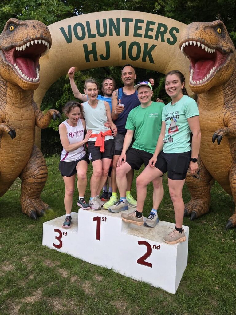 A group of runners standing on a plinth in front of a blow-up dinosaur